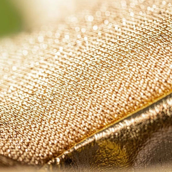 Close-up of a gold glittery textured fabric surface with a diagonal fold and soft blurred background.