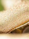 Close-up of a gold glittery textured fabric surface with a diagonal fold and soft blurred background.