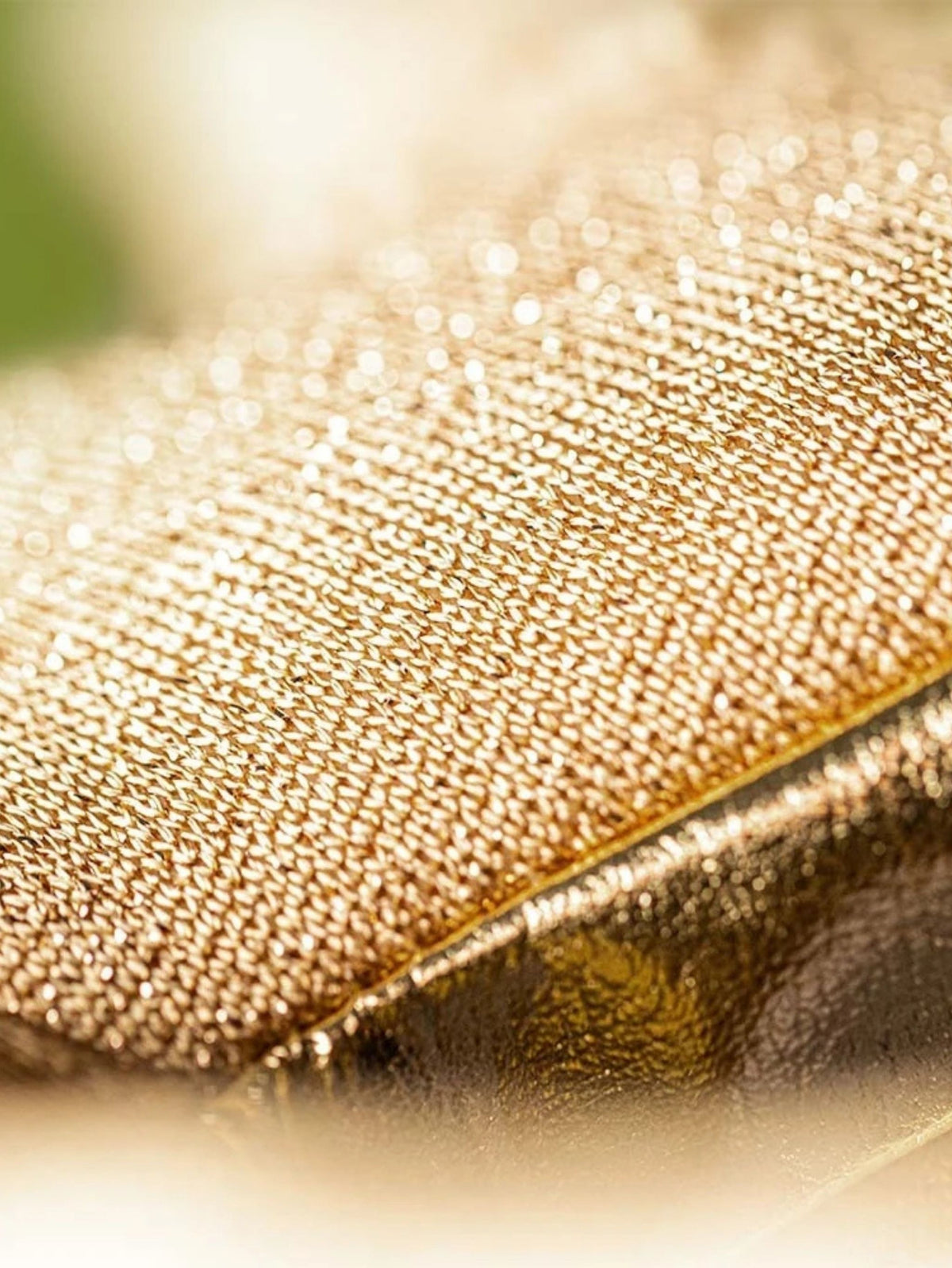 Close-up of a gold glittery textured fabric surface with a diagonal fold and soft blurred background.