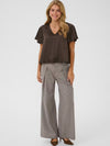 A woman modeling a dark brown short-sleeve V-neck top and light gray wide-leg trousers against a plain light gray studio background.