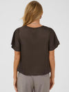 A woman viewed from the back wearing a dark brown short-sleeve blouse with flutter sleeves and gray patterned trousers, against a light gray studio background.