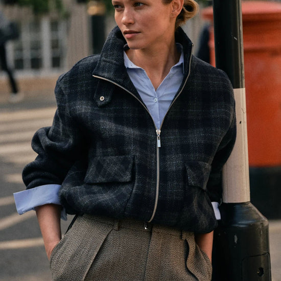 Woman wearing a plaid jacket and light blue shirt on a city street.
