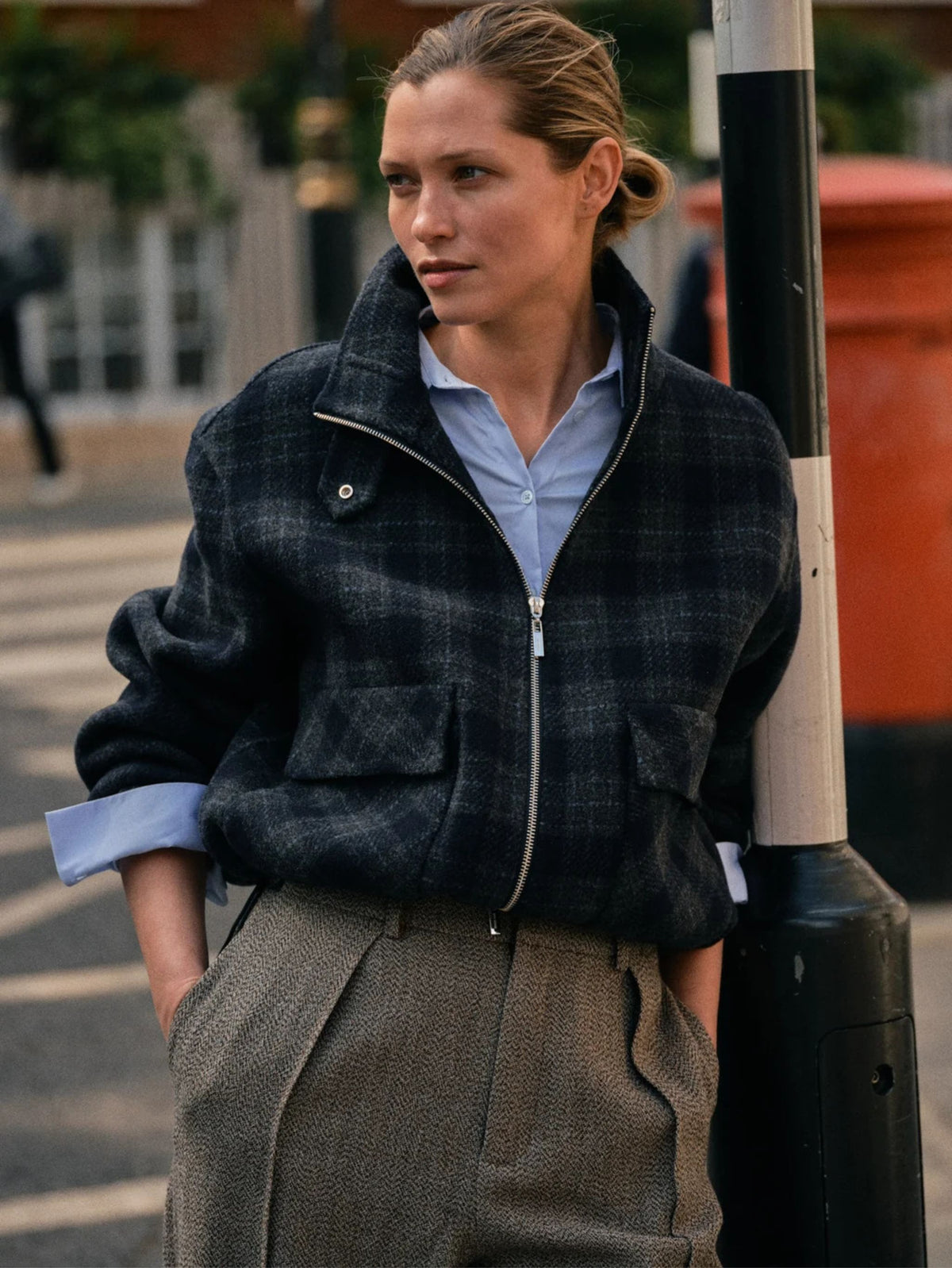 Woman wearing a plaid jacket and light blue shirt on a city street.