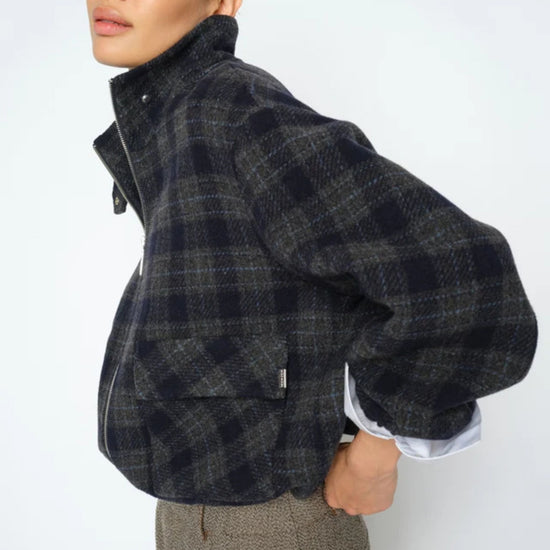 Person wearing a dark plaid jacket with a white shirt underneath on a plain background