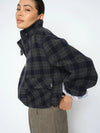 Person wearing a dark plaid jacket with a white shirt underneath on a plain background