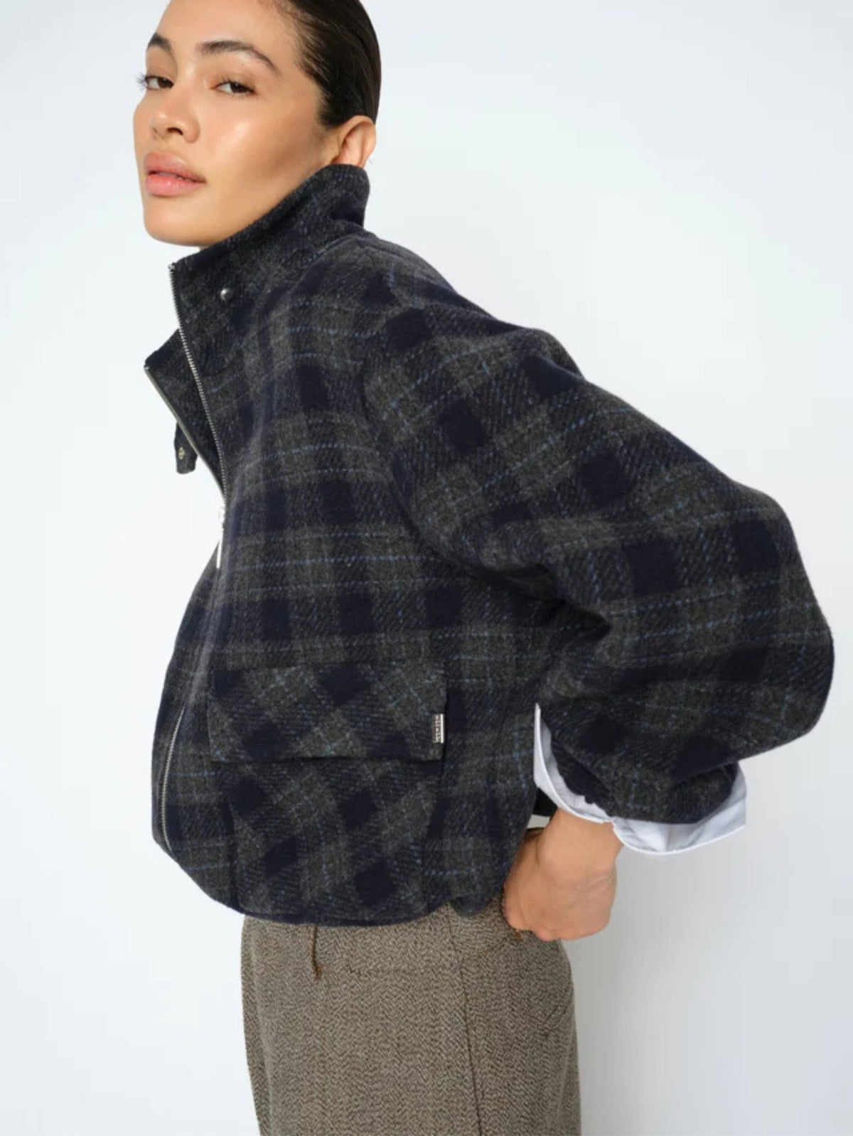 Person wearing a dark plaid jacket with a white shirt underneath on a plain background