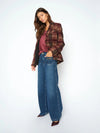 Woman wearing a plaid jacket, purple top, and blue jeans on a white background