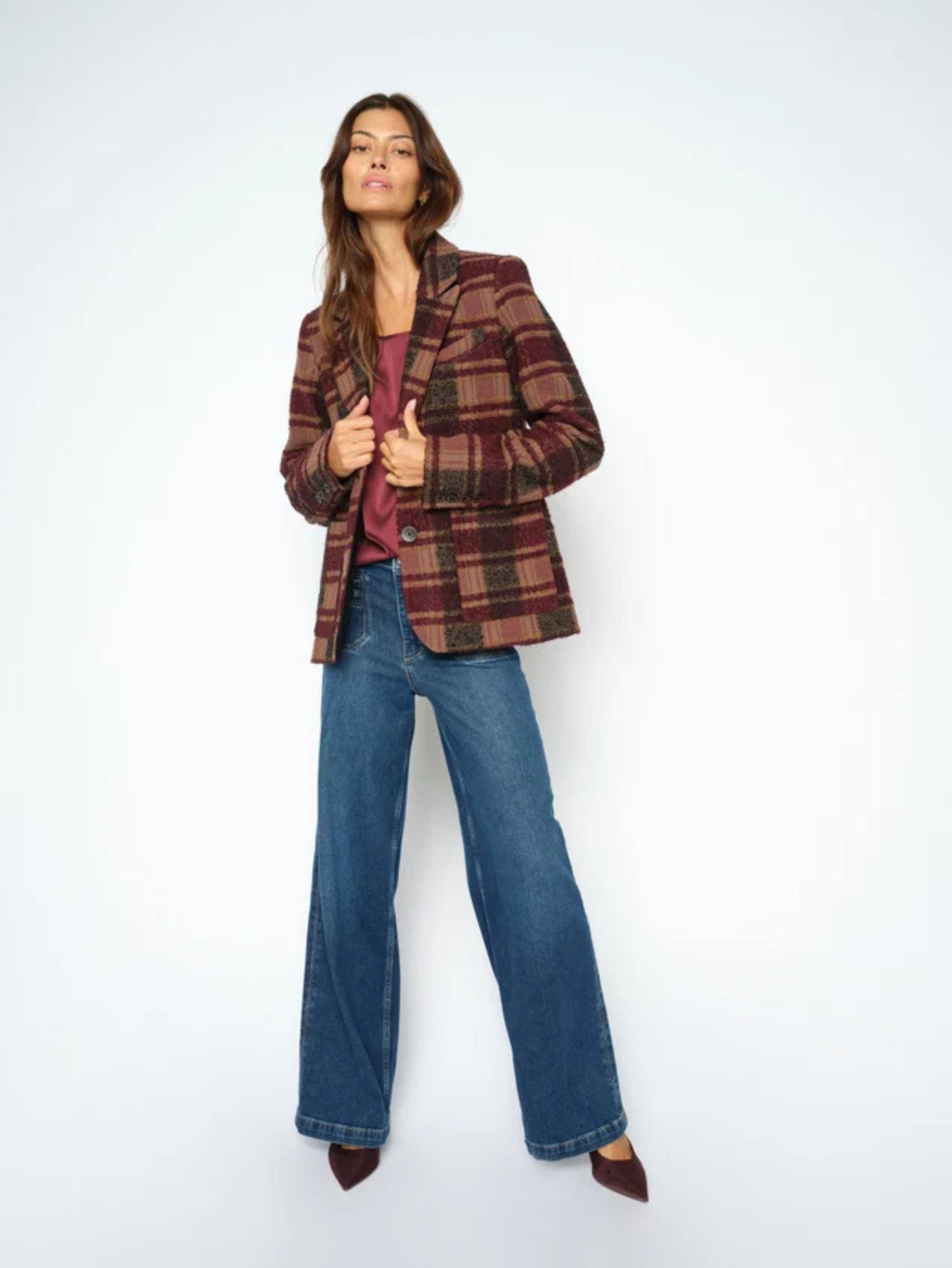 Woman wearing a plaid jacket, purple top, and blue jeans on a white background