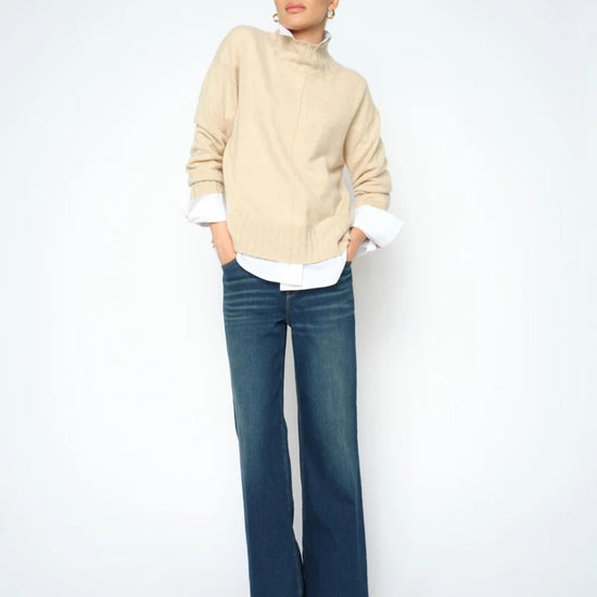 Woman wearing a beige sweater and blue jeans on a white background