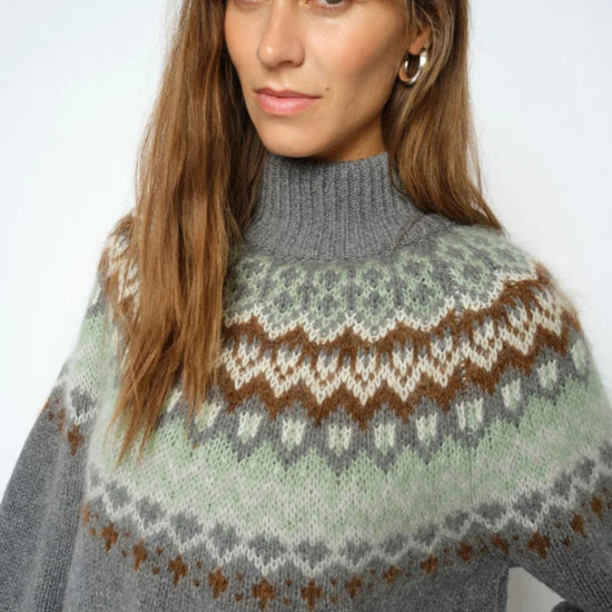 Woman wearing a gray sweater with a patterned design on a plain background