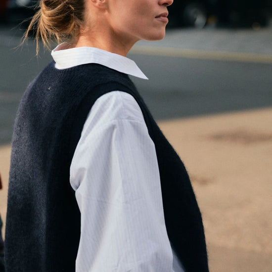 Woman wearing a black vest over a white shirt with a blurred background