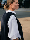 Woman wearing a black vest over a white shirt with a blurred background