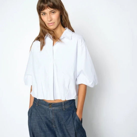 Woman wearing a white shirt and blue jeans against a plain background