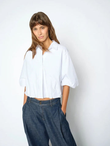 Woman wearing a white shirt and blue jeans against a plain background