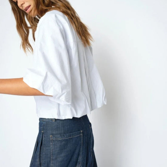 Person wearing a white shirt and blue jeans against a plain background