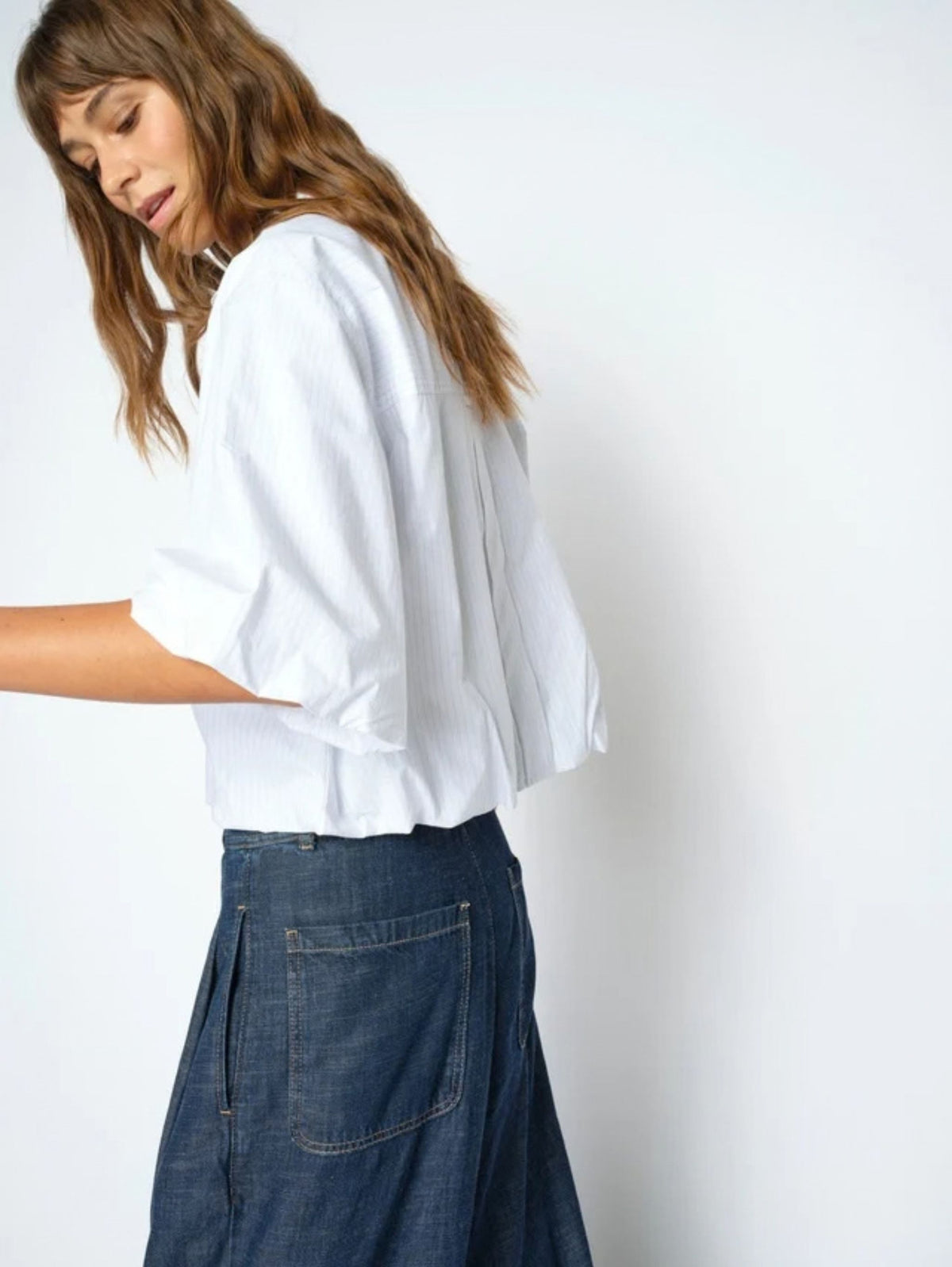 Person wearing a white shirt and blue jeans against a plain background