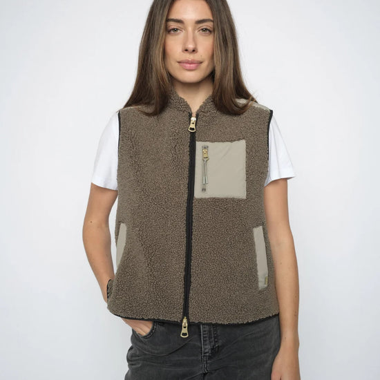 Person wearing a Olive fleece vest with a white shirt and dark jeans on a white background
