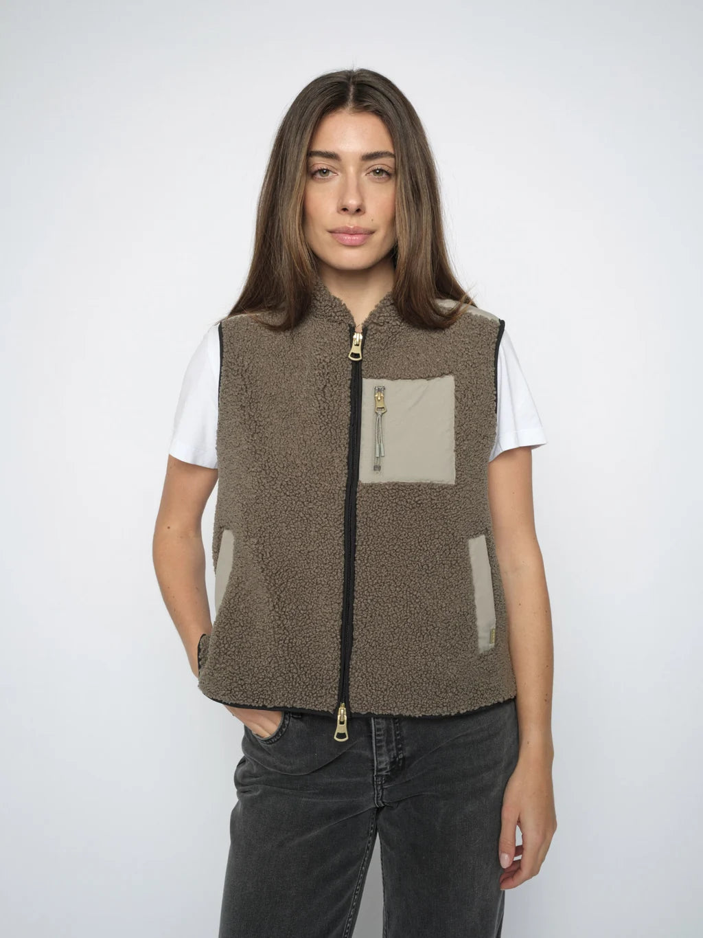 Person wearing a Olive fleece vest with a white shirt and dark jeans on a white background
