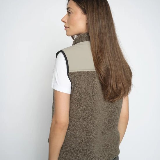 Woman wearing a olive vest over a white shirt on a plain background