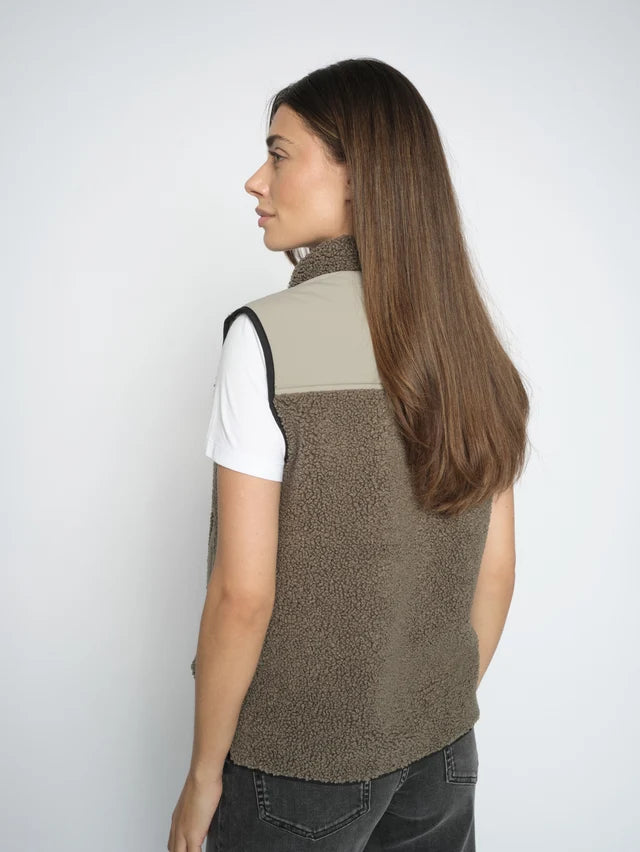 Woman wearing a olive vest over a white shirt on a plain background