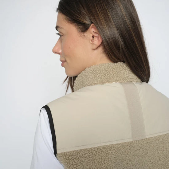 Person wearing a beige fleece vest against a white background