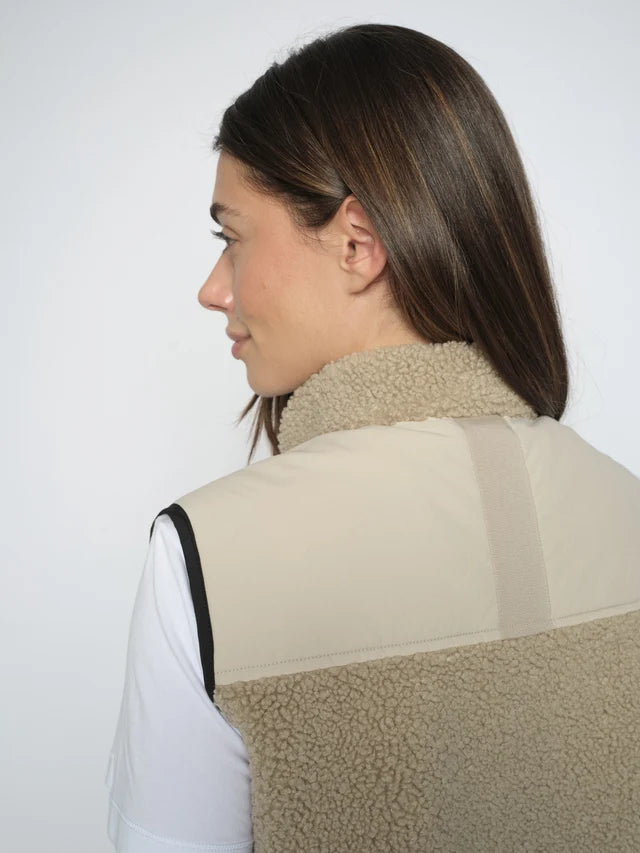Person wearing a beige fleece vest against a white background
