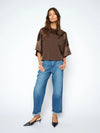 A woman modeling a brown short-sleeve top with sheer mesh sleeves and wide cuffs, paired with blue jeans and black slingback heels, against a plain white studio background.