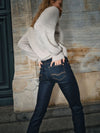 Person wearing a light gray sweater and dark blue jeans against a textured stone wall.