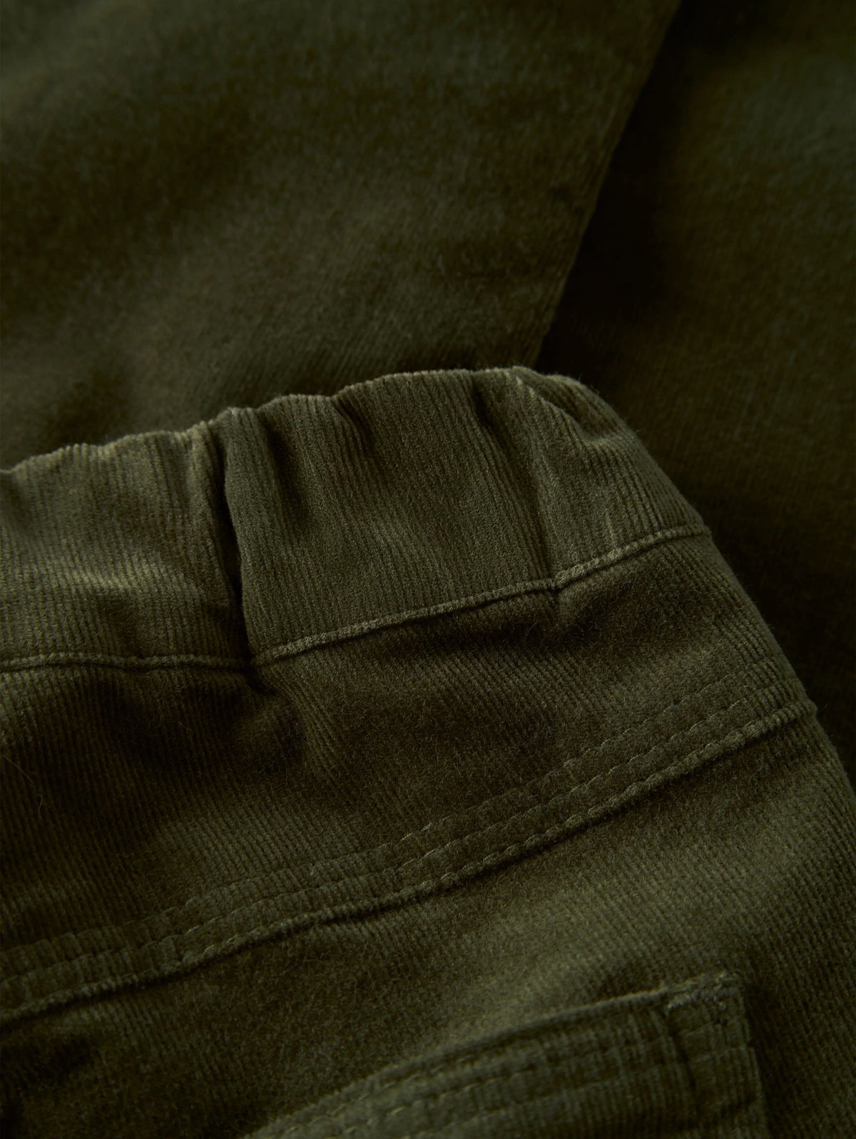 Close-up of dark olive green corduroy fabric showing the ribbed texture and stitched seam details.