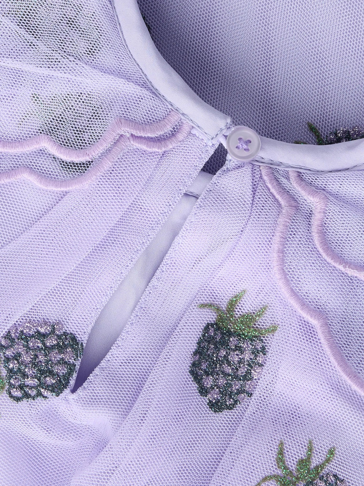 Close-up of a light lavender mesh garment with scalloped embroidered trim and embroidered pineapple motifs in green and lavender.
