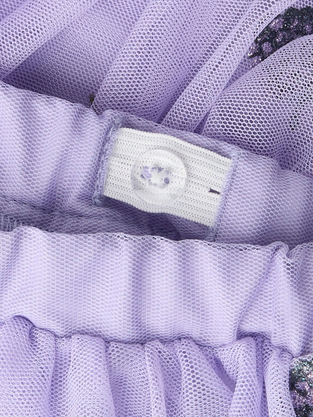 Close-up of a lavender purple mesh garment with a white button closure and ruffled trim.