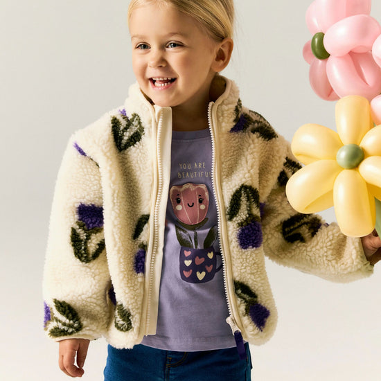 Child wearing a floral-patterned jacket holding balloons against a plain background