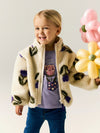 Child wearing a floral-patterned jacket holding balloons against a plain background