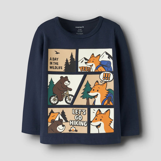 A navy blue long-sleeve t-shirt for kids, featuring a large cartoon comic-style graphic on the front with foxes, bears, trees, mountains, and text like 'A DAY IN THE WILDLIFE' and 'LET'S GO HIKING'.