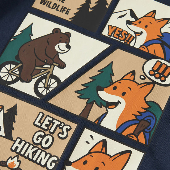 Close-up of a navy blue garment featuring a large cartoon-style multicolor graphic print with panels showing a bear on a bicycle, foxes, trees, campfire, and text reading 'A DAY IN THE WILDLIFE' and 'LET'S GO HIKING'.