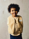 A boy standing in a beige sleeveless teddybear vest against a grey background