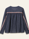 A dark blue denim long-sleeve blouse with a gathered waist and embroidered floral details along the neckline and down the sleeves, shown against a light cream background.