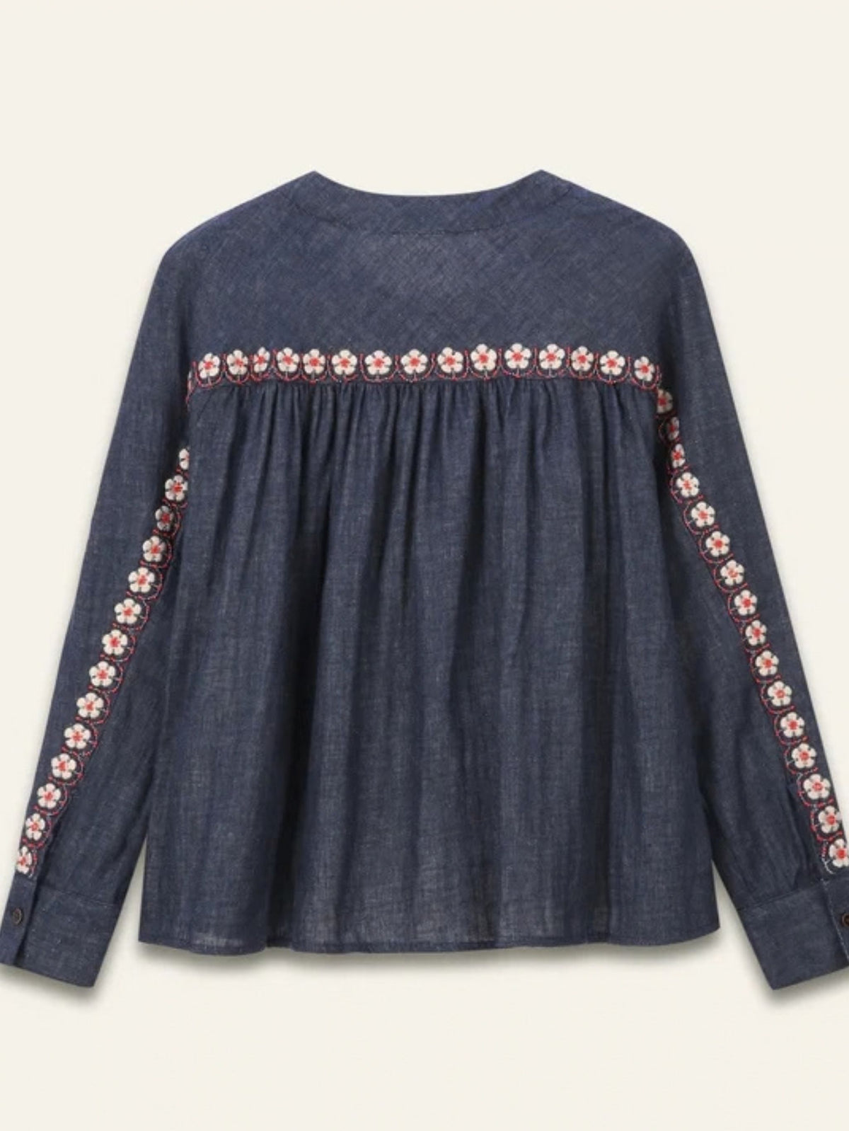A dark blue denim long-sleeve blouse with a gathered waist and embroidered floral details along the neckline and down the sleeves, shown against a light cream background.