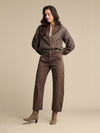 A woman modeling a brown leopard-print long-sleeve blouse and brown straight-leg pants, paired with taupe ankle boots, against a solid beige studio background.