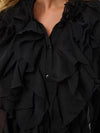 Close-up of a black ruffled blouse with layered cascading ruffles, a split neckline, and dark buttons, shown on a model.