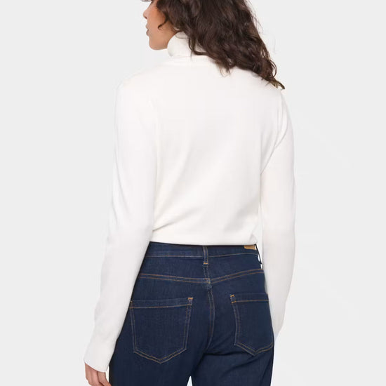 A woman shown from the back wearing a white mock-neck long-sleeve top and dark blue jeans against a light gray studio background.