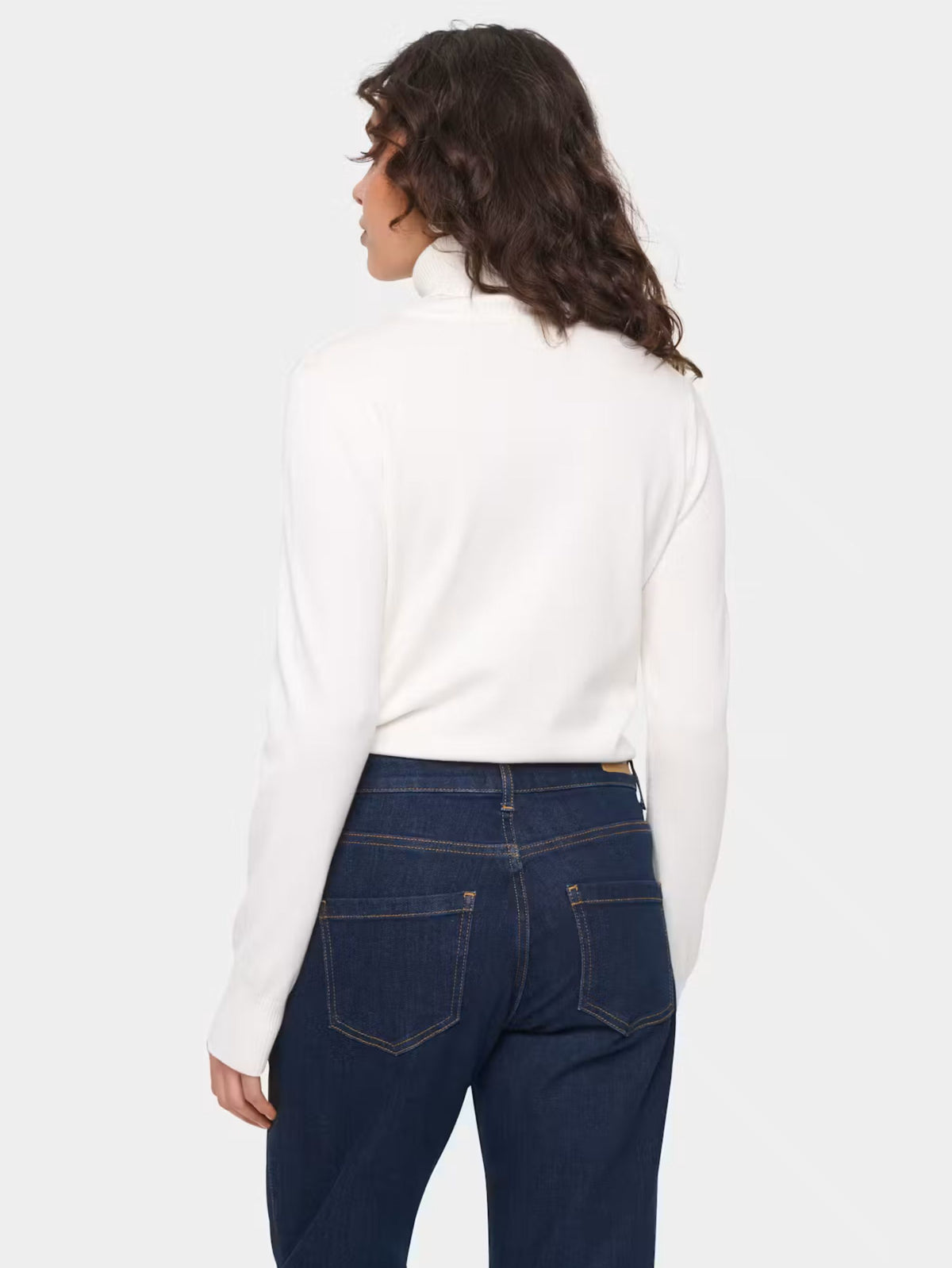 A woman shown from the back wearing a white mock-neck long-sleeve top and dark blue jeans against a light gray studio background.
