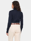 A woman shown from the back wearing a dark navy long-sleeve turtleneck sweater, cream-colored trousers, and a brown leather belt, against a light gray studio background.