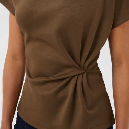 A close-up of a person wearing a short-sleeve brown top with a twisted knot detail at the waist, paired with dark blue jeans against a light gray background.