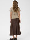 A woman shown from the back wearing a beige short-sleeve t-shirt and a dark brown midi skirt, paired with black flat shoes, against a light gray studio background.