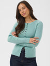 A woman modeling a light blue ribbed knit sweater with a buttoned front and scalloped hem, paired with dark blue jeans against a plain light gray background.