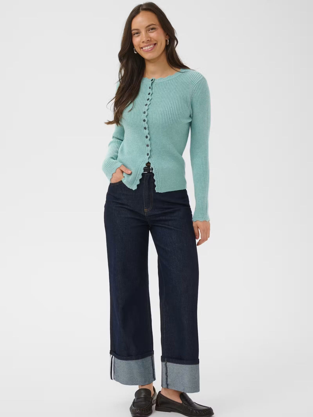 A woman modeling a light aqua ribbed knit cardigan with front buttons, paired with dark blue wide-leg jeans with rolled cuffs and black loafers, against a plain white studio background.