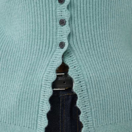 Close-up of a aqua ribbed knit cardigan with dark buttons, worn over dark blue jeans.