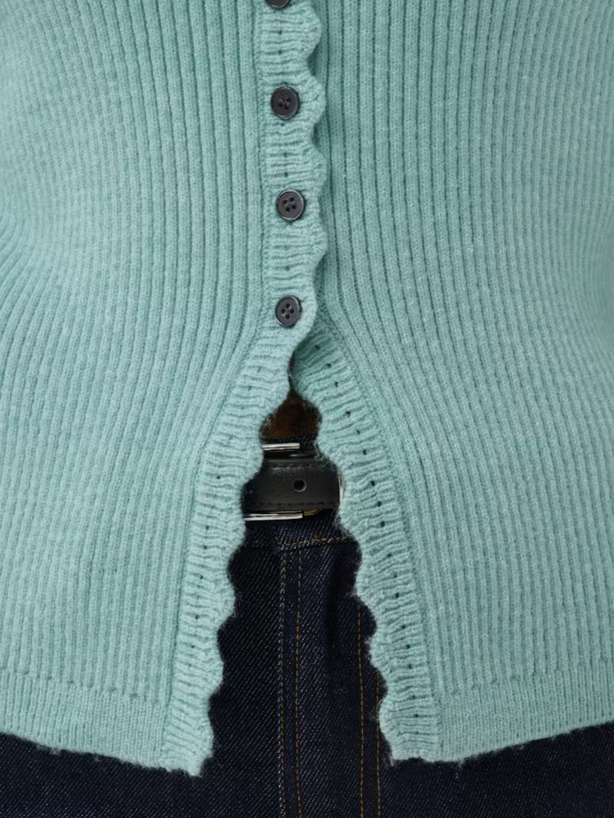 Close-up of a aqua ribbed knit cardigan with dark buttons, worn over dark blue jeans.