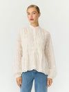 A woman modeling a cream-colored, long-sleeved lace blouse with a high mock neck and gathered peplum hem, paired with blue jeans, against a plain white studio background.